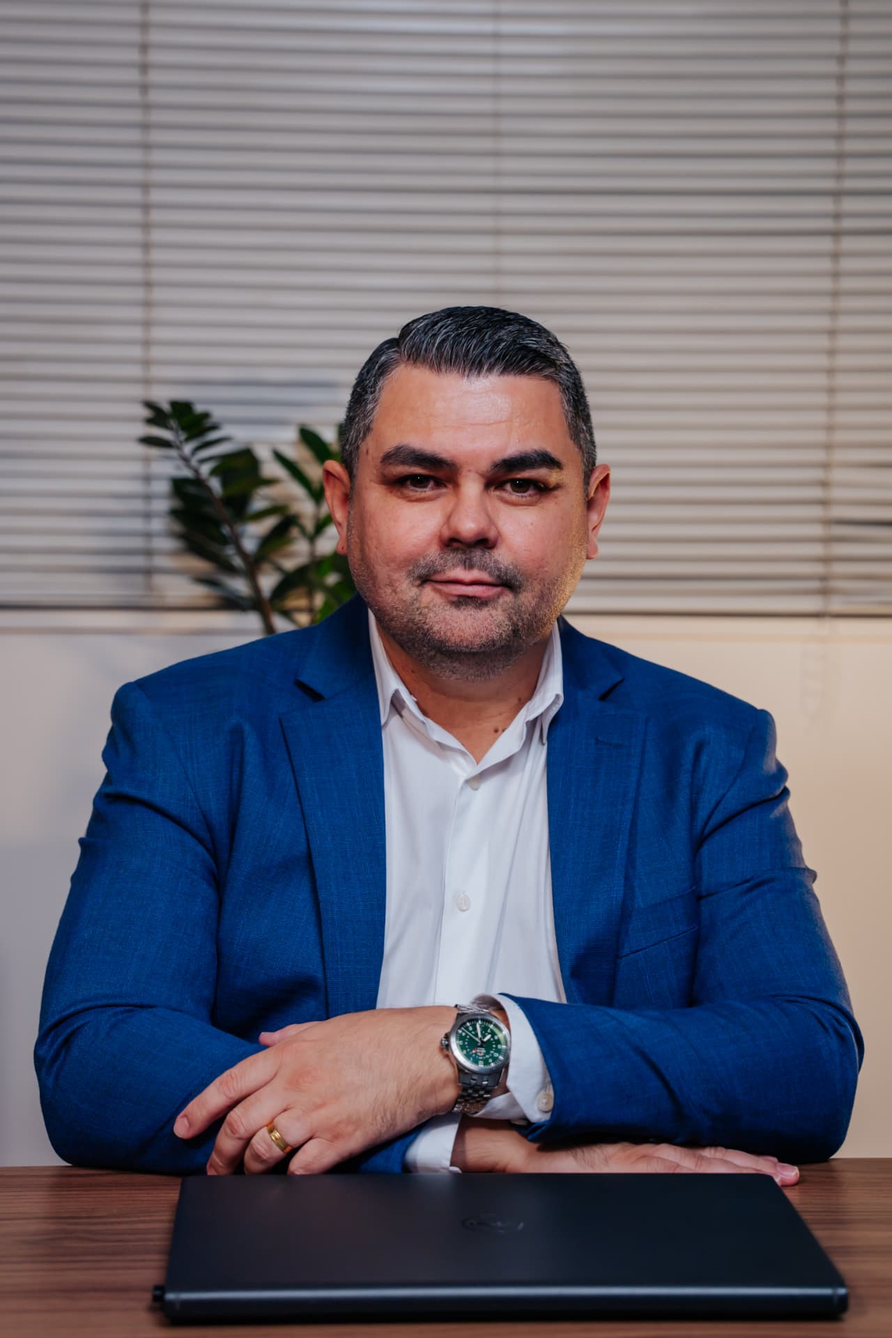 Aldir Silva sentado à mesa, com blazer azul